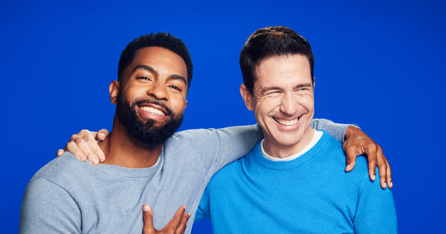 Cropped image of two men in blue sweaters smiling on a blue background.