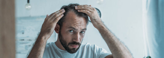 Man with light brown hair and beard wearing a t-shirt inspecting his hairline in the mirror.