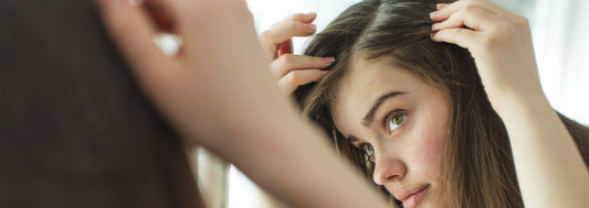 Woman with long, light brown hair checking her part in the mirror.