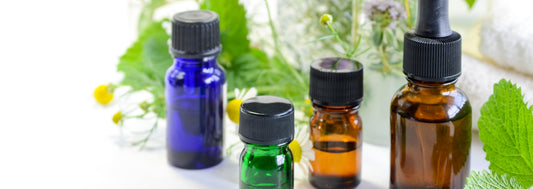Small glass bottles of oils in different colors with a black cap surrounded by fresh daises on a white background.