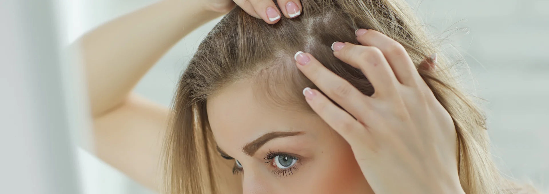 Woman with long blond hair checking her part in the mirror.