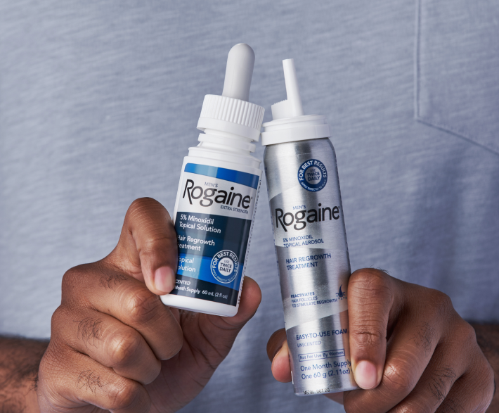 Two hands, each holding a Rogaine product. Serum on the left, foam on the right.